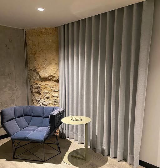 Cortina panel gris junto a silla azul y muro de piedra